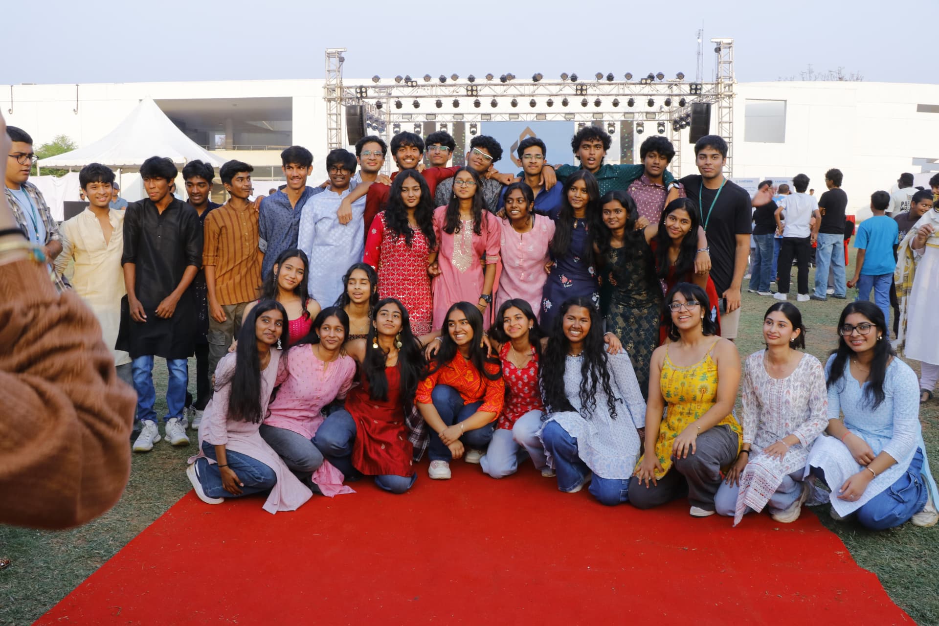 Large group of students and organisers posing on a red carpet in front of the Fiesta stage